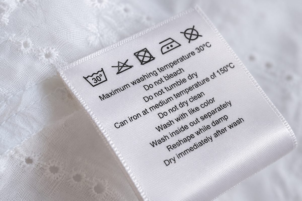 Satin care label with ISO care symbols and full wash instructions on a white eyelet garment