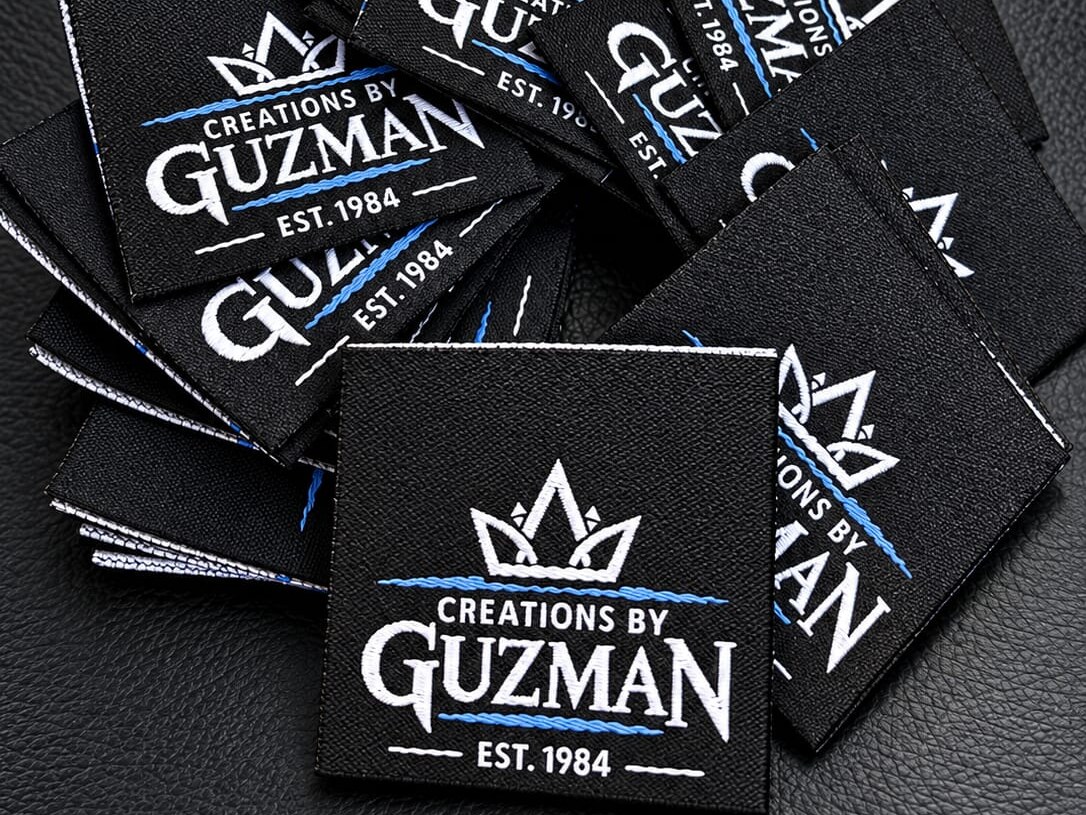 Black woven labels with white and blue Creations by Guzman artwork