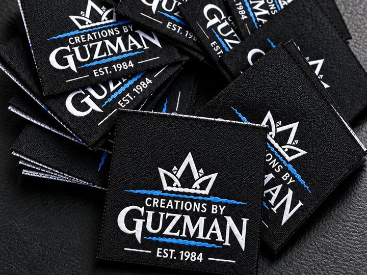 Stack of black Creations by Guzman woven labels with a white crown logo