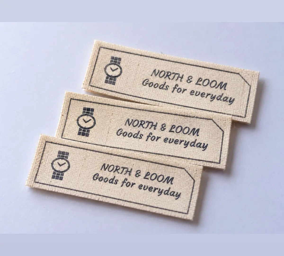 Natural cream North and Loom woven labels with a navy watch emblem